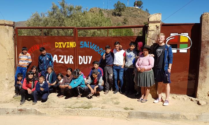Das Bild zeigt eine Gruppe junger Menschen in Bolivien. Es ist ein Gruppenbild vor einem Tor.
