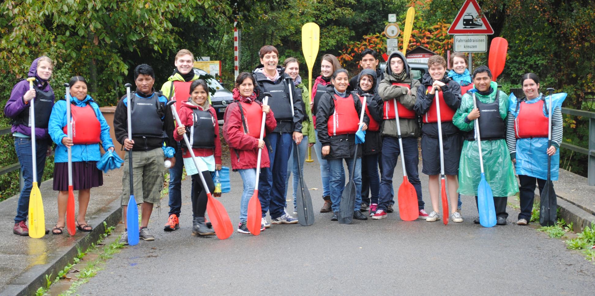 Das Bild zeigt eine Gruppe junger Personen. Alle halten Paddel in der Hand