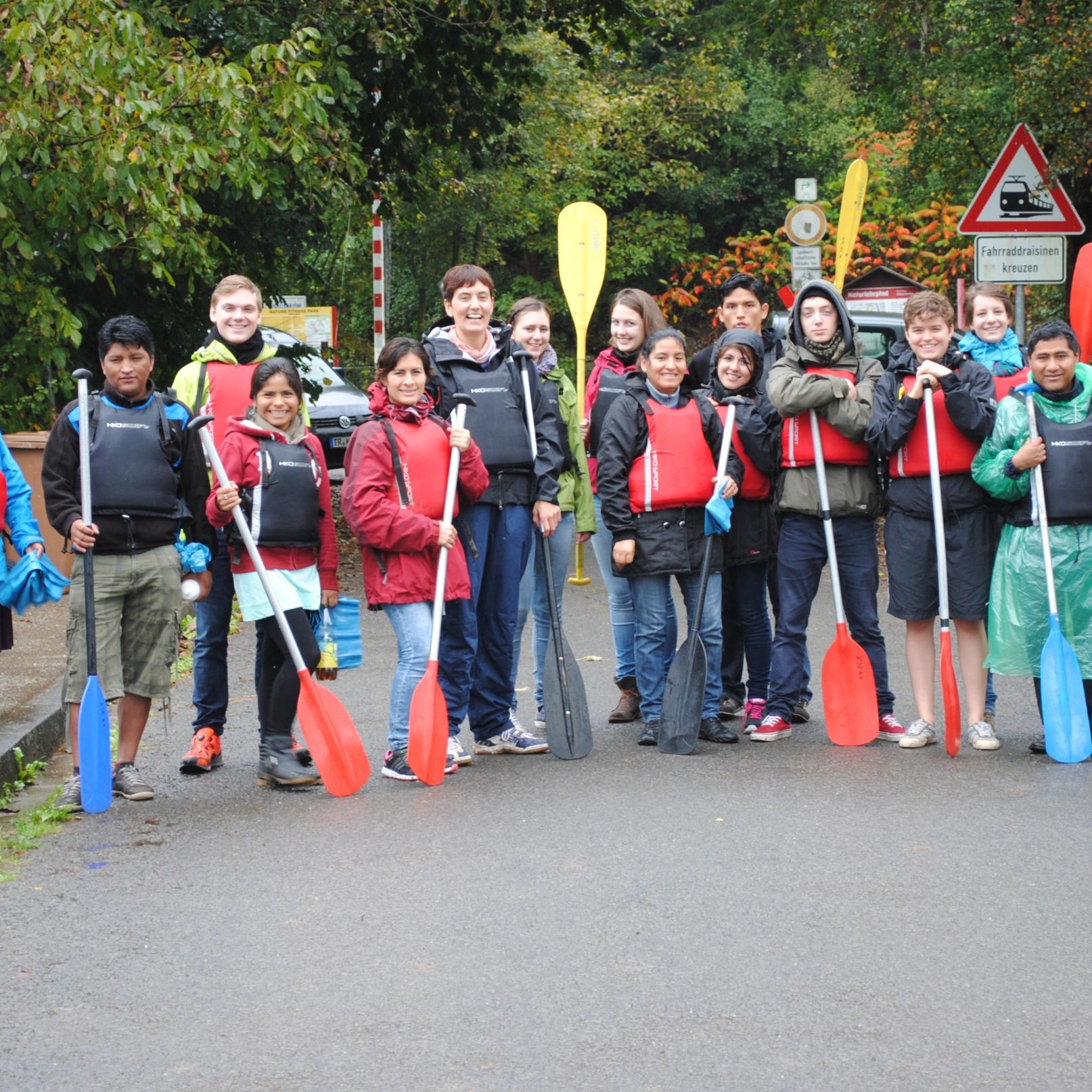Das Bild zeigt eine Gruppe junger Personen. Alle halten Paddel in der Hand