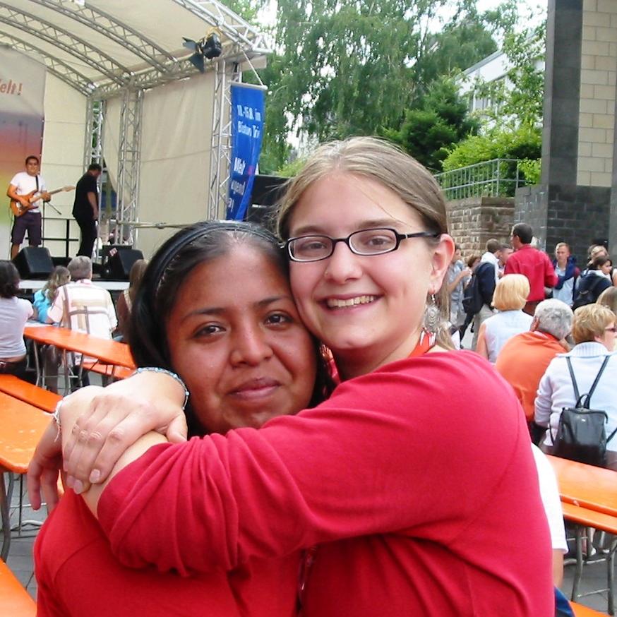 Das Bild zeigt zwei junge Damen, welche sich vor einer Bühne umarmen