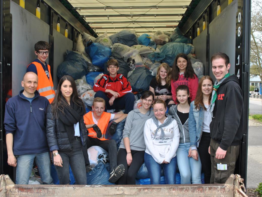 Das Bild zeigt eine Gruppe junger Menschen auf der Laderampe eines LKWs. Er ist voll mit Kleidersäcken beladen.