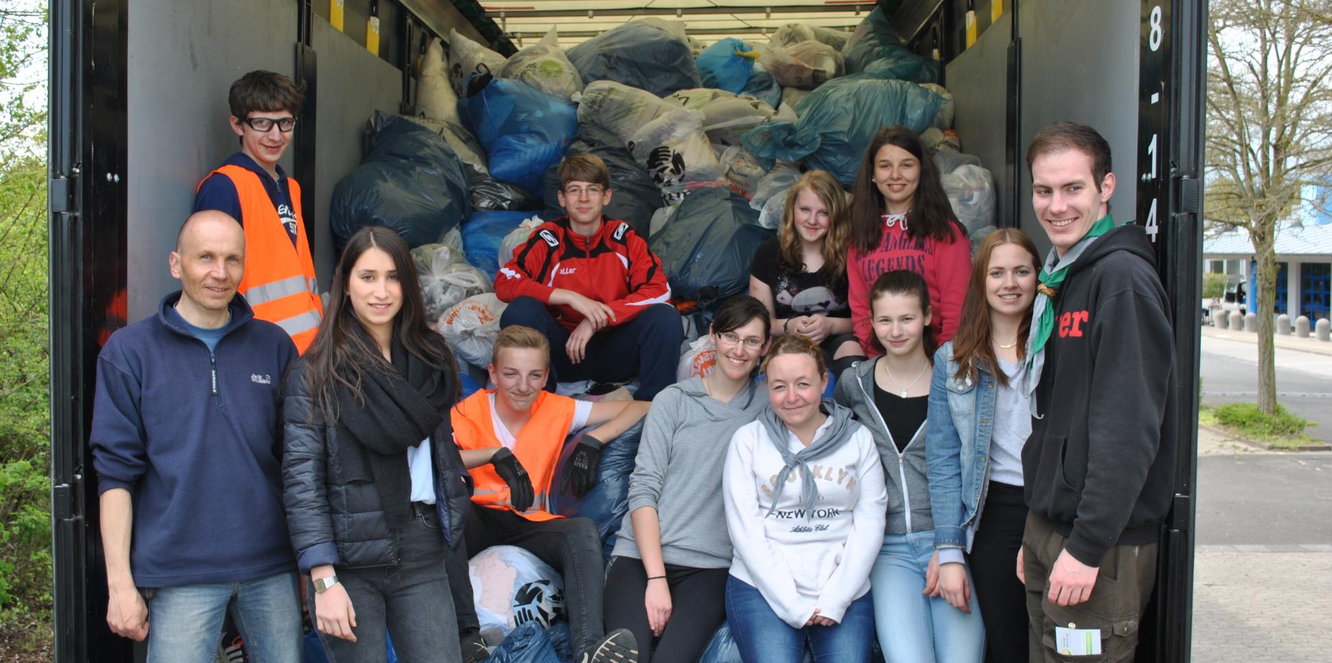 Das Bild zeigt eine Gruppe junger Menschen auf der Laderampe eines LKWs. Er ist voll mit Kleidersäcken beladen.