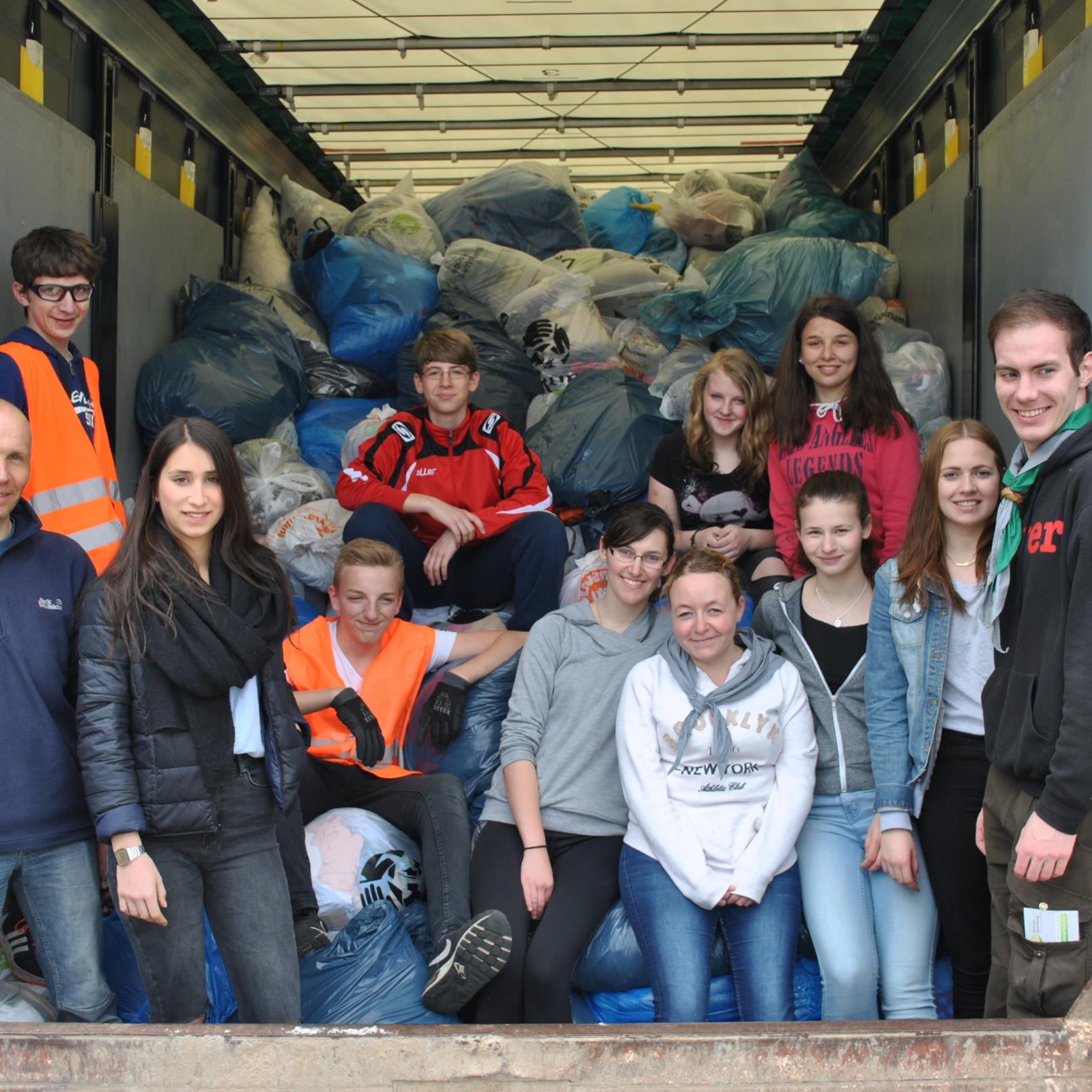 Das Bild zeigt eine Gruppe junger Menschen auf der Laderampe eines LKWs. Er ist voll mit Kleidersäcken beladen.