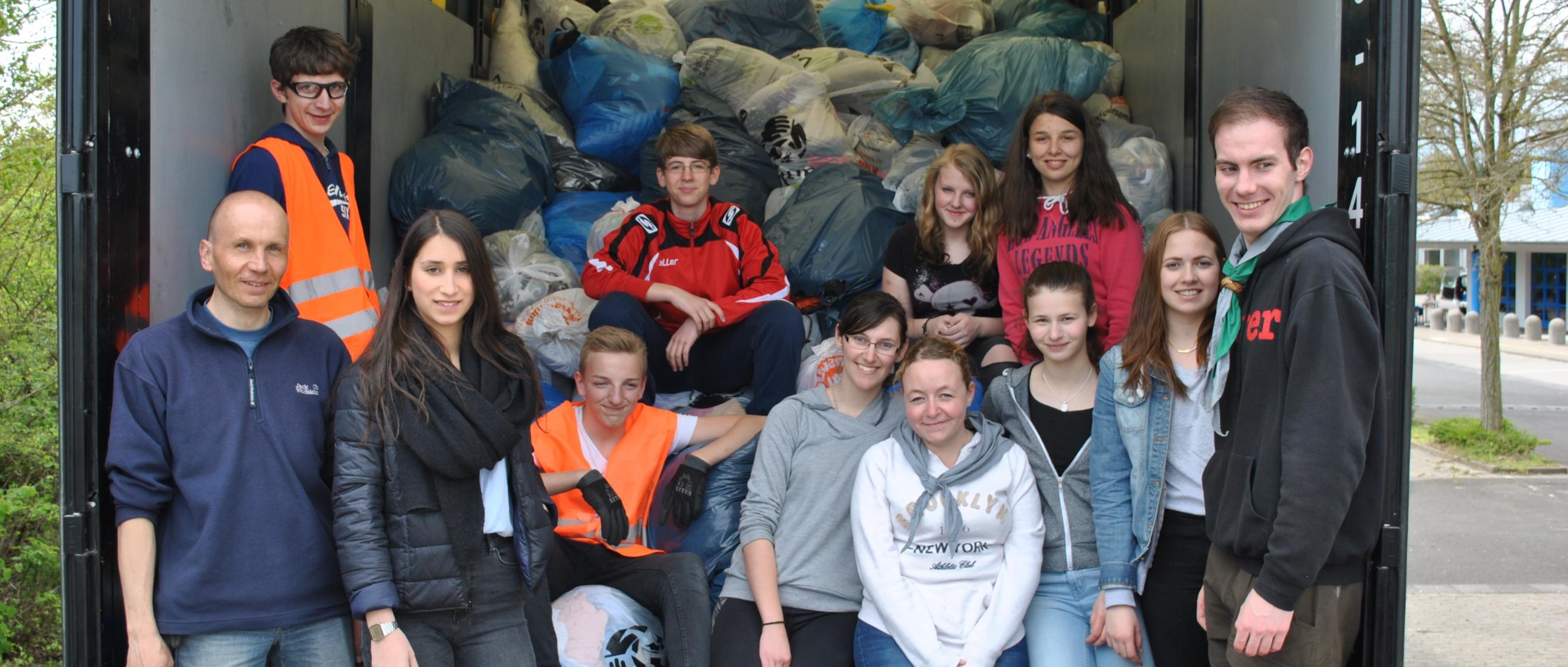 Das Bild zeigt eine Gruppe junger Menschen auf der Laderampe eines LKWs. Er ist voll mit Kleidersäcken beladen.