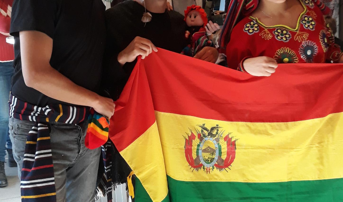 Das Bild zeigt  Bolivianische Freiwillige beim 2nd Hemd & Hose Markt. Sie halten eine Fahne von Bolivien hoch.