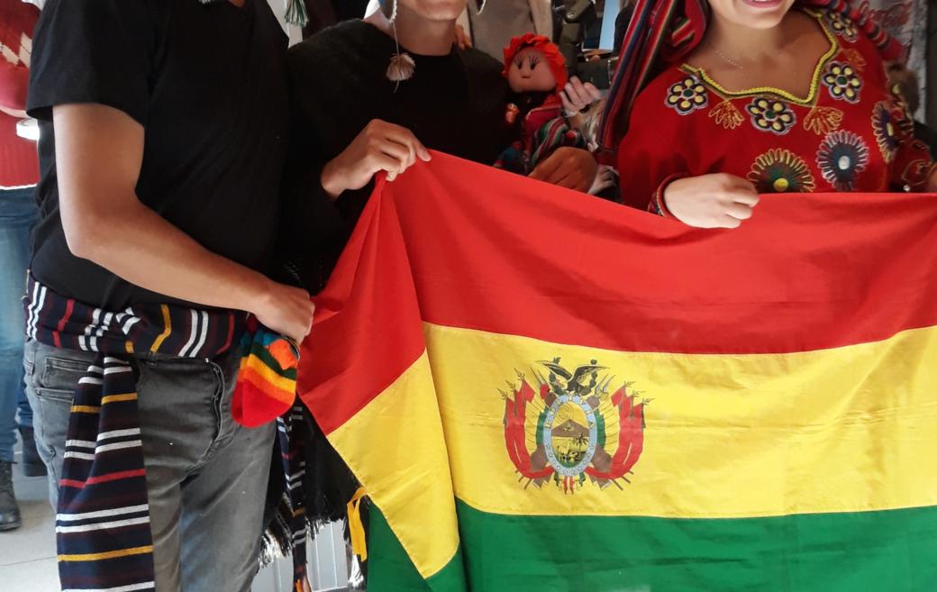 Das Bild zeigt  Bolivianische Freiwillige beim 2nd Hemd & Hose Markt. Sie halten eine Fahne von Bolivien hoch.