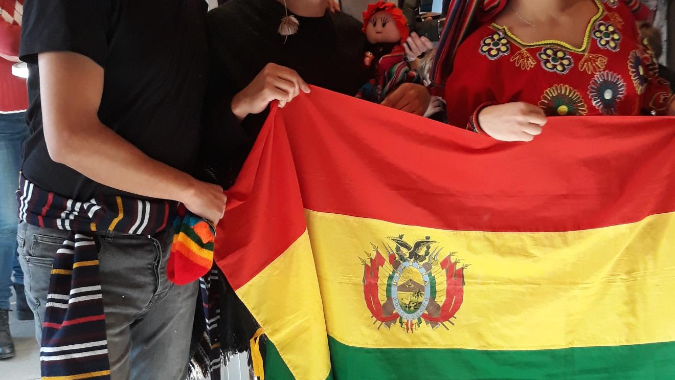 Das Bild zeigt  Bolivianische Freiwillige beim 2nd Hemd & Hose Markt. Sie halten eine Fahne von Bolivien hoch.