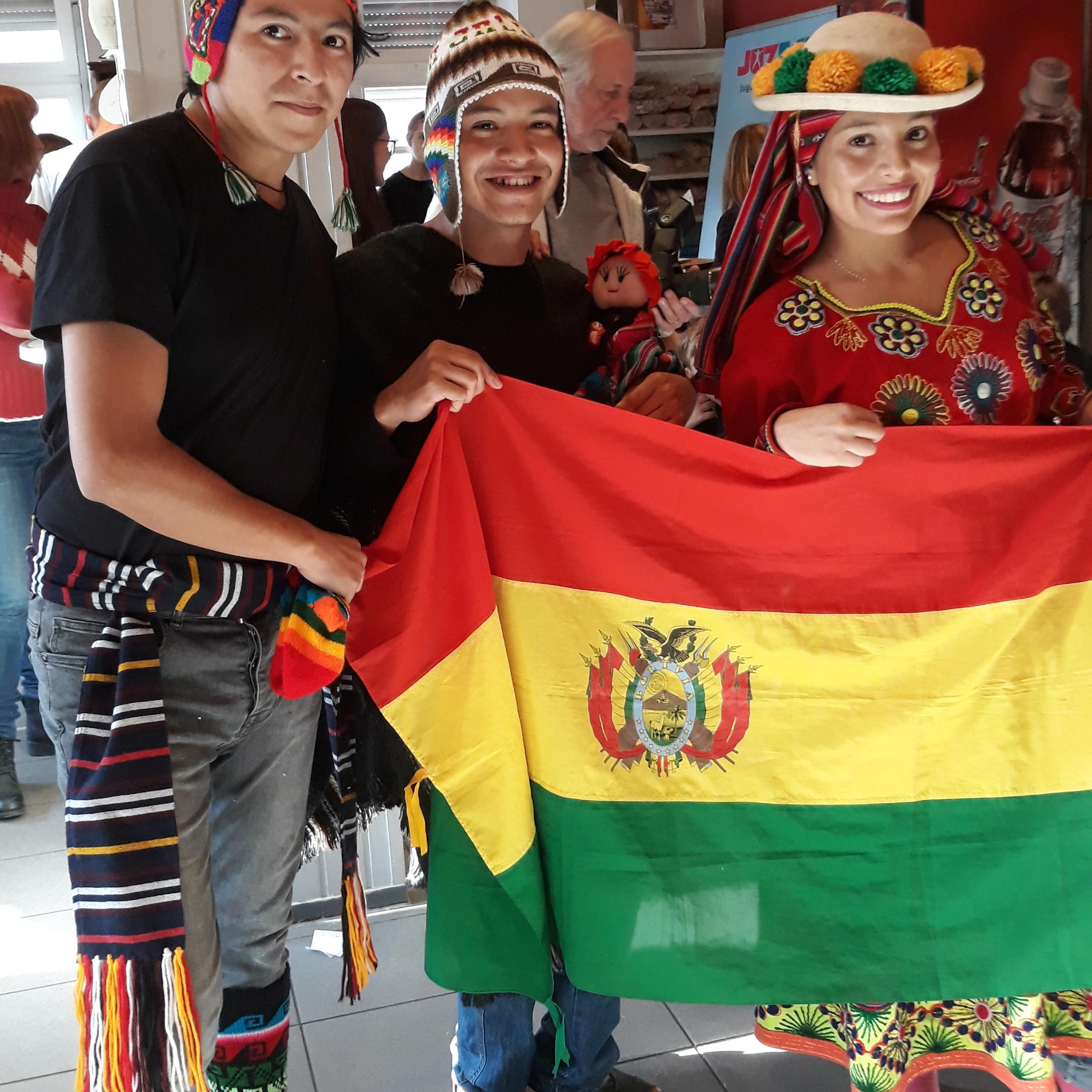 Das Bild zeigt  Bolivianische Freiwillige beim 2nd Hemd & Hose Markt. Sie halten eine Fahne von Bolivien hoch.