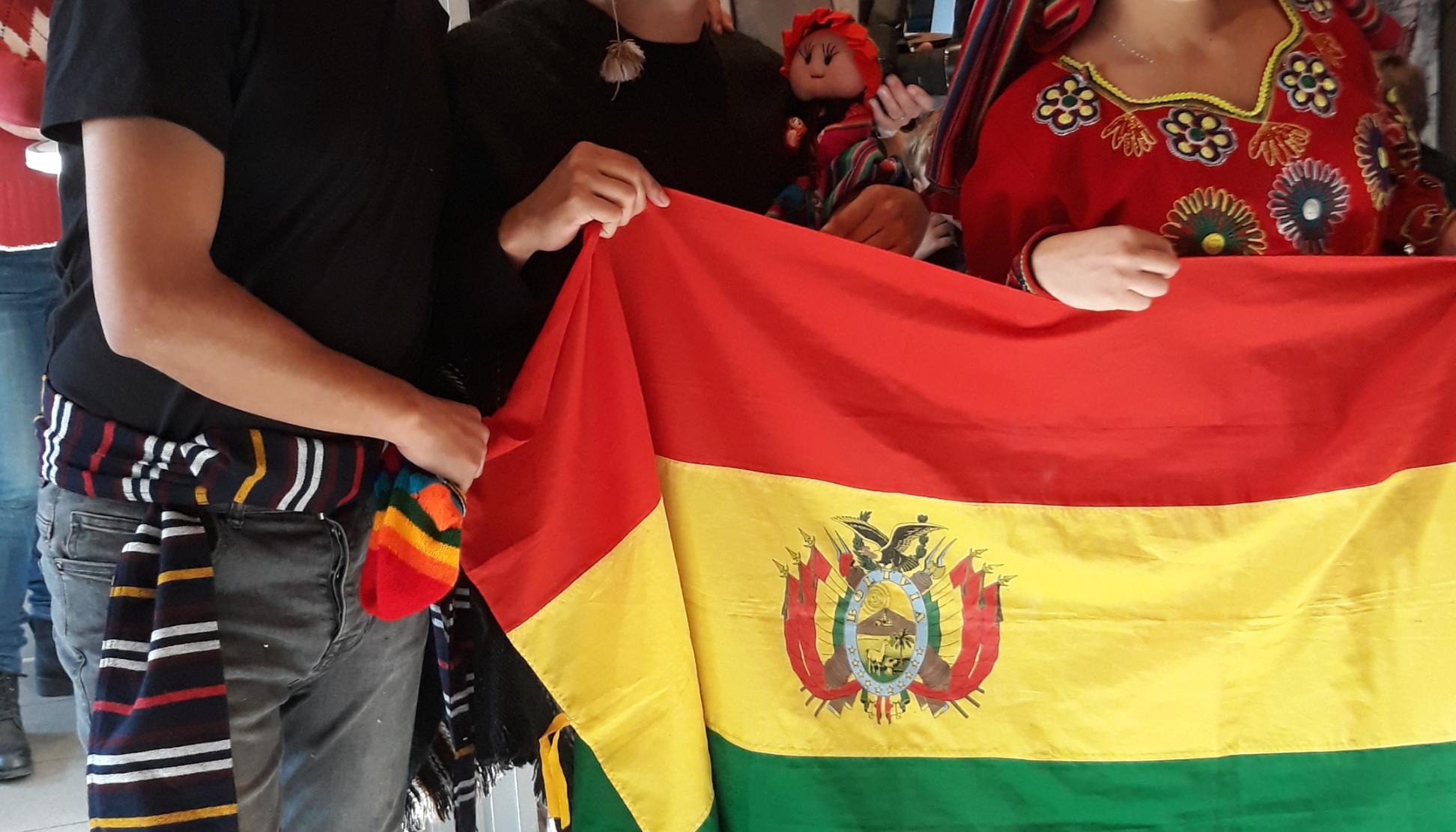 Das Bild zeigt  Bolivianische Freiwillige beim 2nd Hemd & Hose Markt. Sie halten eine Fahne von Bolivien hoch.