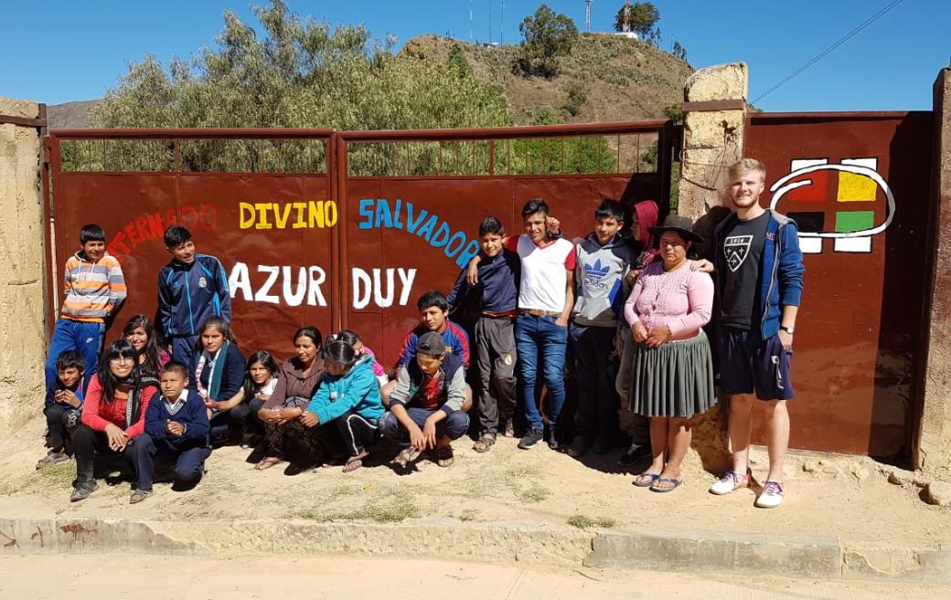 Das Bild zeigt eine Gruppe junger Menschen in Bolivien. Es ist ein Gruppenbild vor einem Tor.