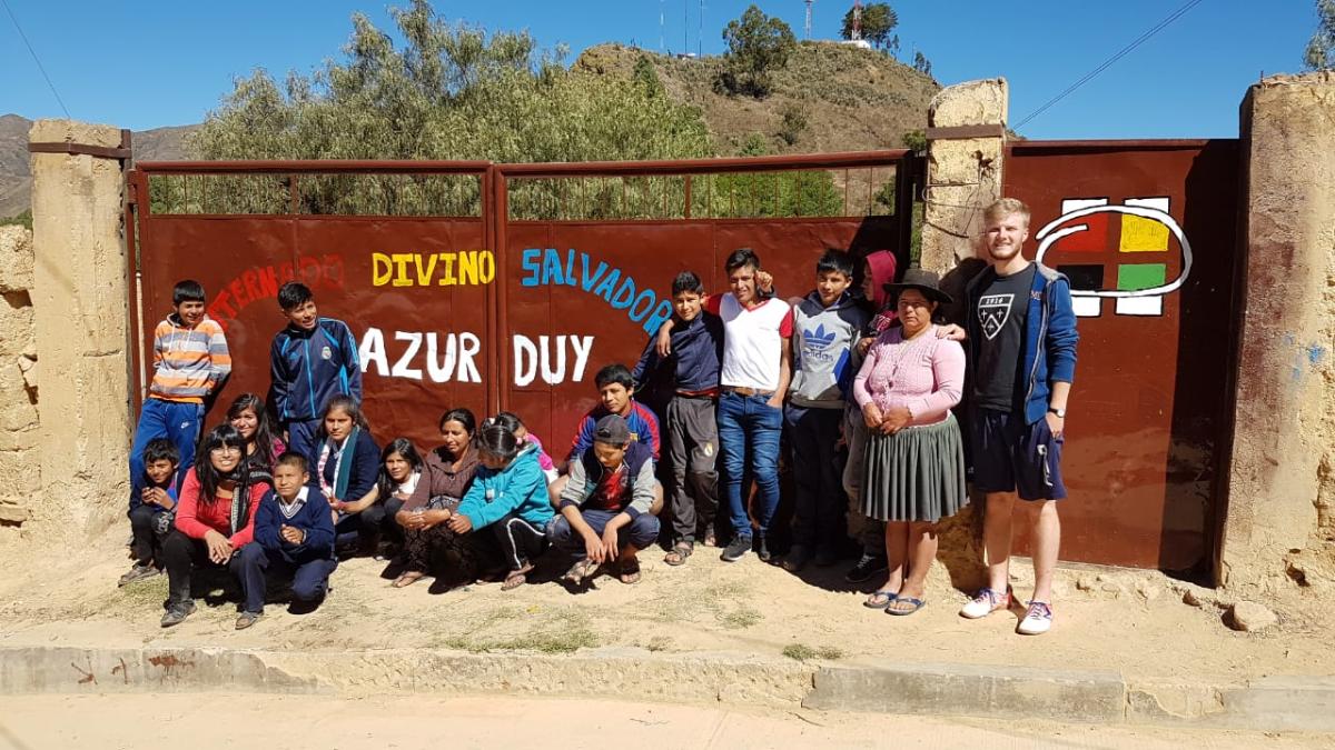 Das Bild zeigt eine Gruppe junger Menschen in Bolivien. Es ist ein Gruppenbild vor einem Tor.