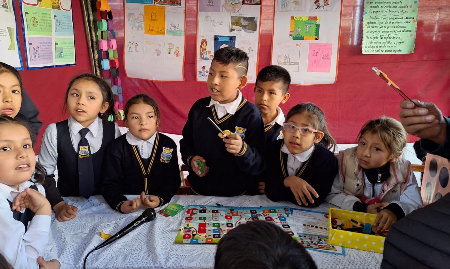 Das Bild zeigt Kinder in Bolivien in einer Schule. Im Hintergrund hängen von ihnen gestaltete Plakate