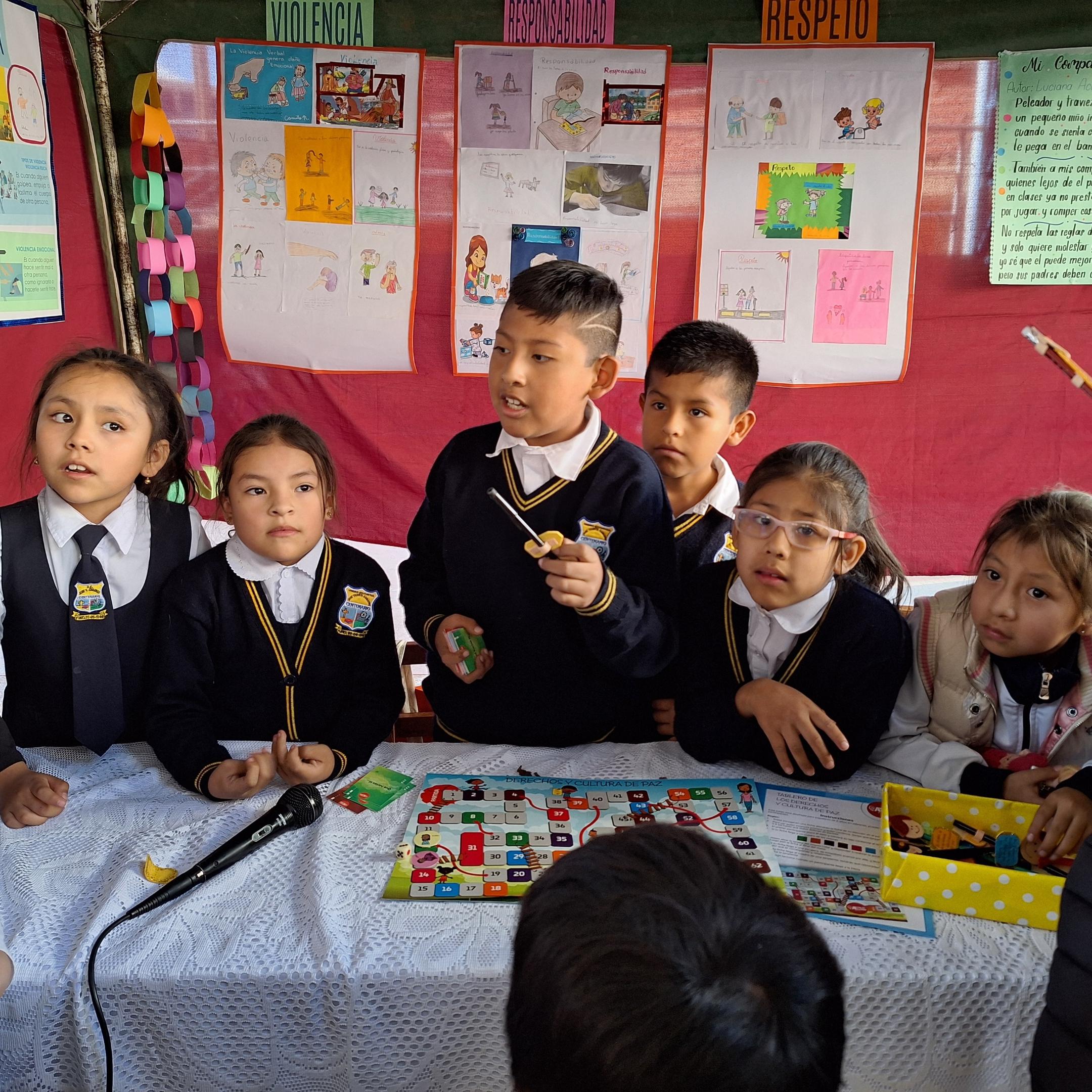 Das Bild zeigt Kinder in Bolivien in einer Schule. Im Hintergrund hängen von ihnen gestaltete Plakate