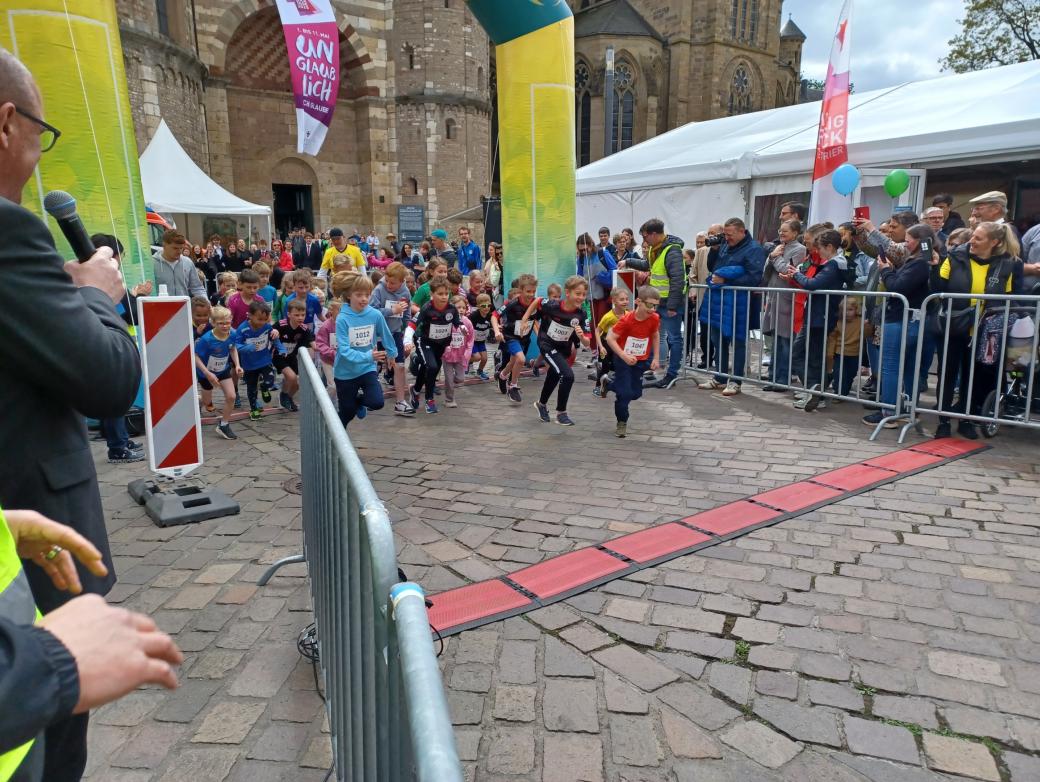 Das Bild zeigt den Start eines Spendenlaufes vor dem Trierer Dom. Man sieht viele Läufer.