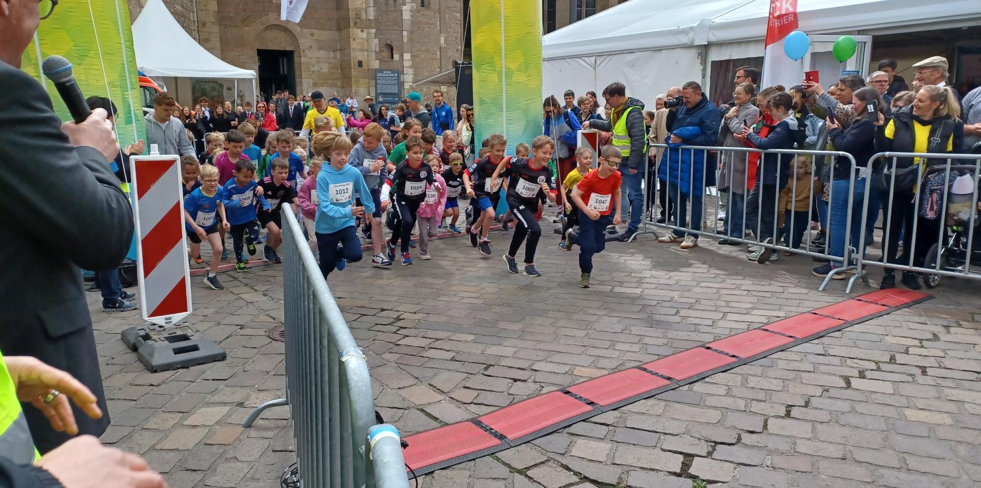 Das Bild zeigt den Start eines Spendenlaufes vor dem Trierer Dom. Man sieht viele Läufer.