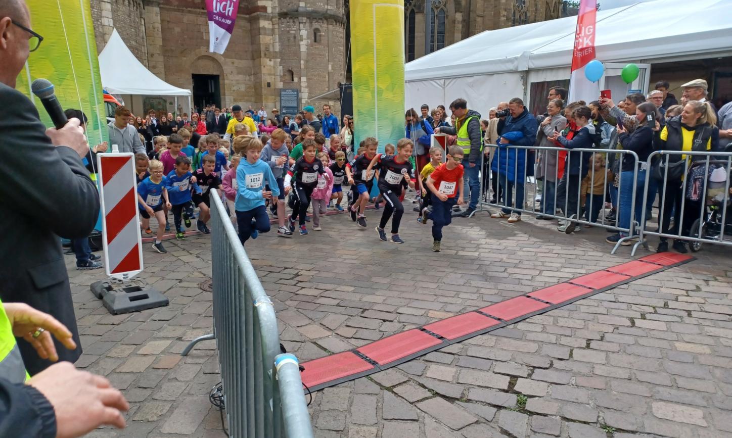 Das Bild zeigt den Start eines Spendenlaufes vor dem Trierer Dom. Man sieht viele Läufer.