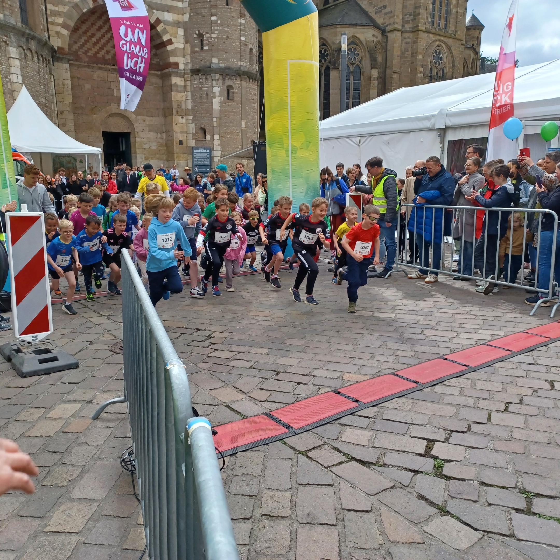 Das Bild zeigt den Start eines Spendenlaufes vor dem Trierer Dom. Man sieht viele Läufer.