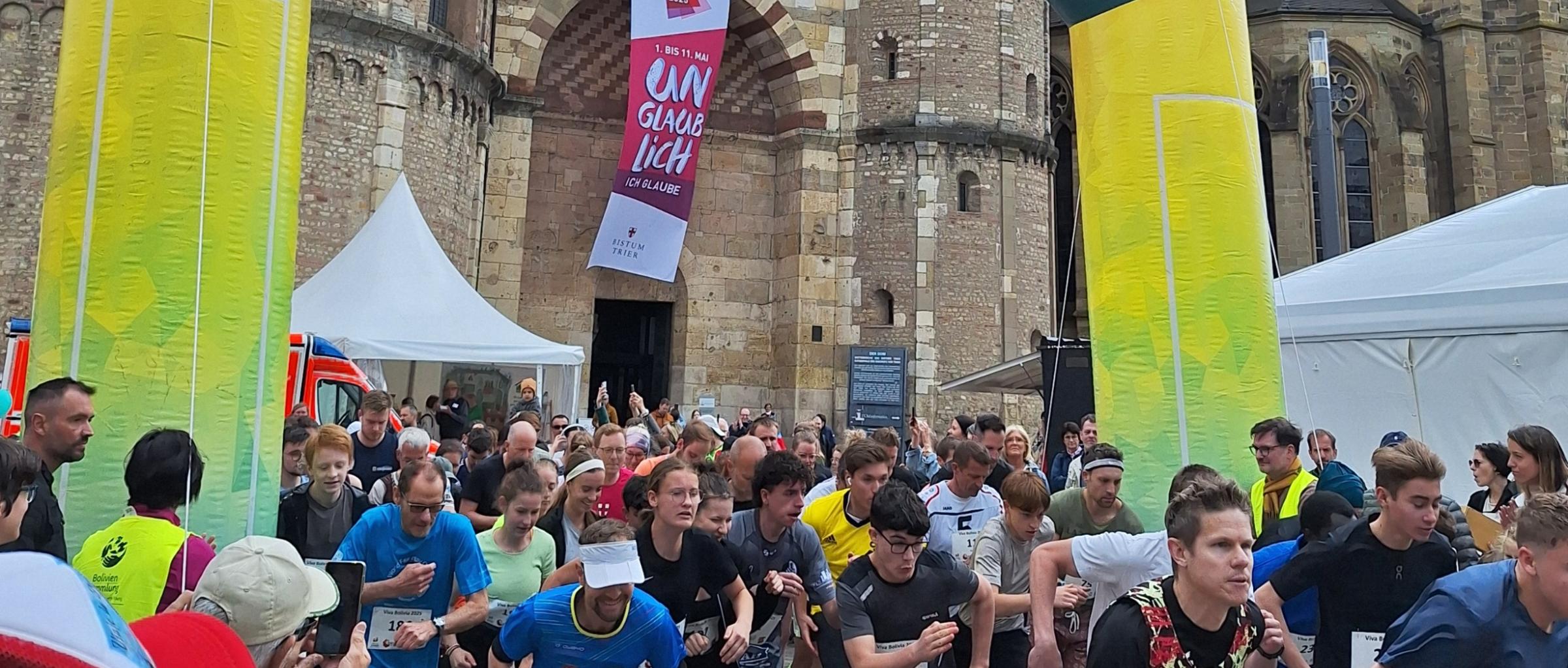 Das Bild zeigt das Ziel eines Spendenlaufes vor dem Trierer Dom. Man sieht viele Läufer.