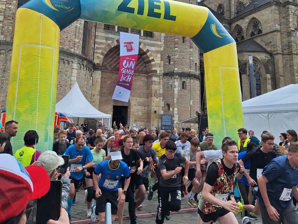 Das Bild zeigt das Ziel eines Spendenlaufes vor dem Trierer Dom. Man sieht viele Läufer.