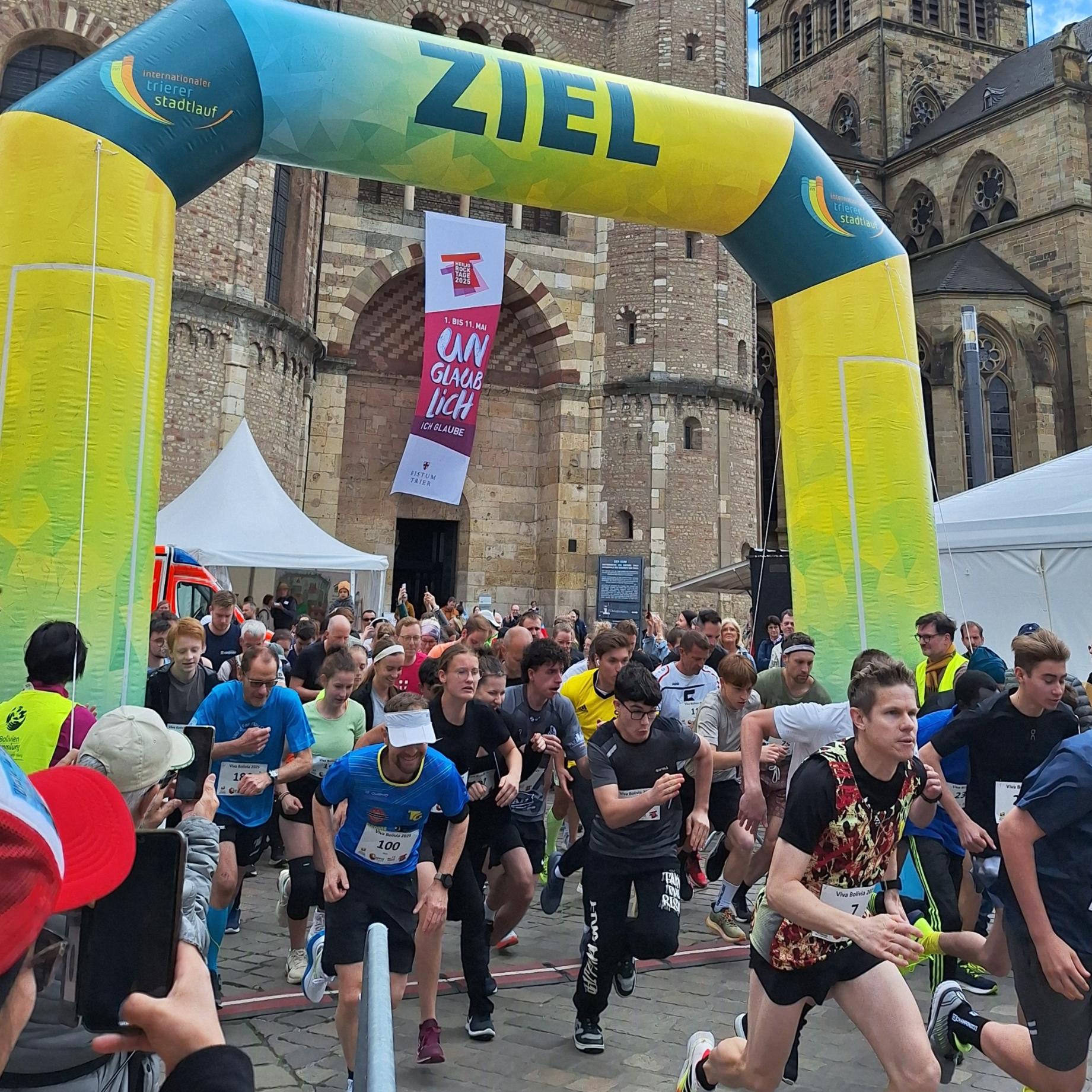 Das Bild zeigt das Ziel eines Spendenlaufes vor dem Trierer Dom. Man sieht viele Läufer.