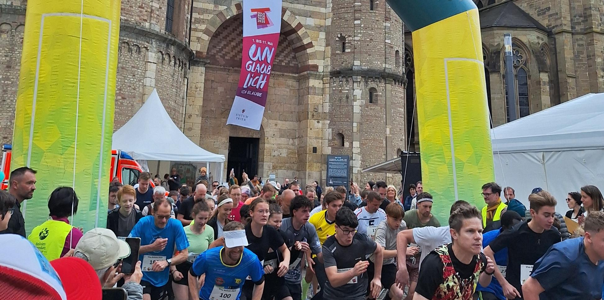 Das Bild zeigt das Ziel eines Spendenlaufes vor dem Trierer Dom. Man sieht viele Läufer.