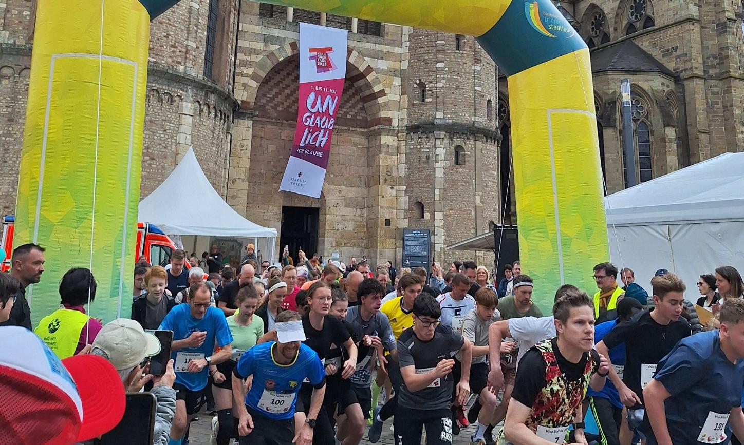 Das Bild zeigt das Ziel eines Spendenlaufes vor dem Trierer Dom. Man sieht viele Läufer.