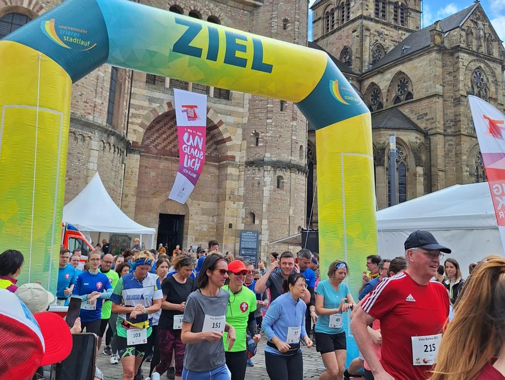 Das Bild zeigt das Ziel eines Spendenlaufes vor dem Trierer Dom. Man sieht viele Läufer.
