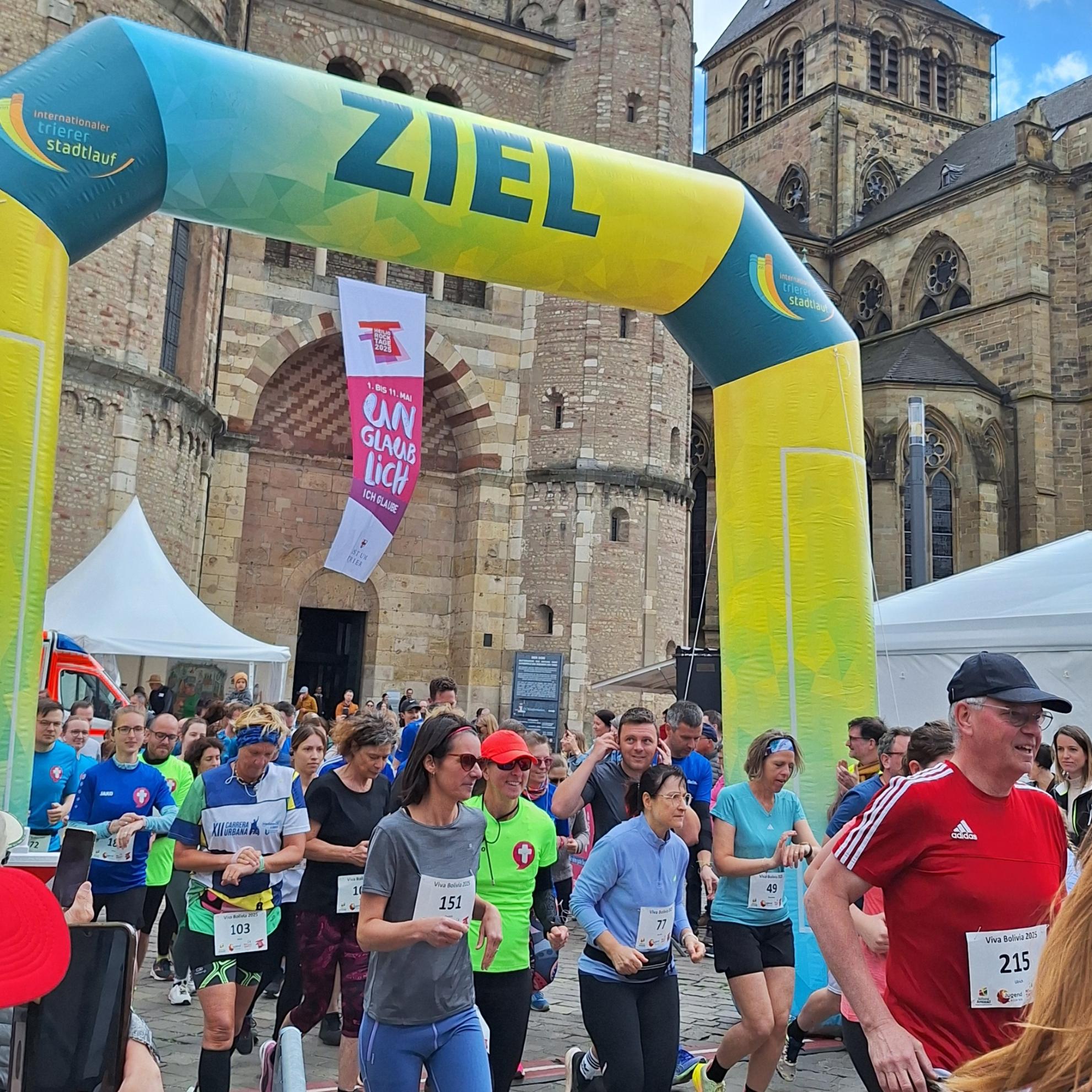 Das Bild zeigt das Ziel eines Spendenlaufes vor dem Trierer Dom. Man sieht viele Läufer.