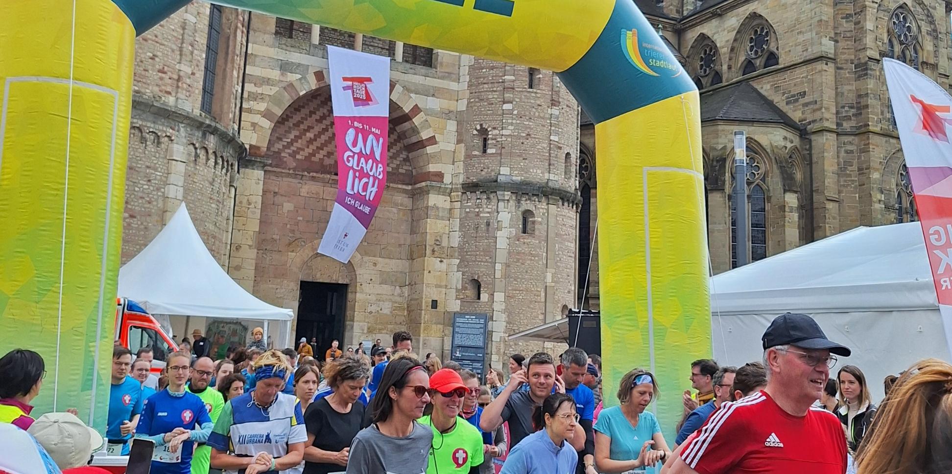 Das Bild zeigt das Ziel eines Spendenlaufes vor dem Trierer Dom. Man sieht viele Läufer.