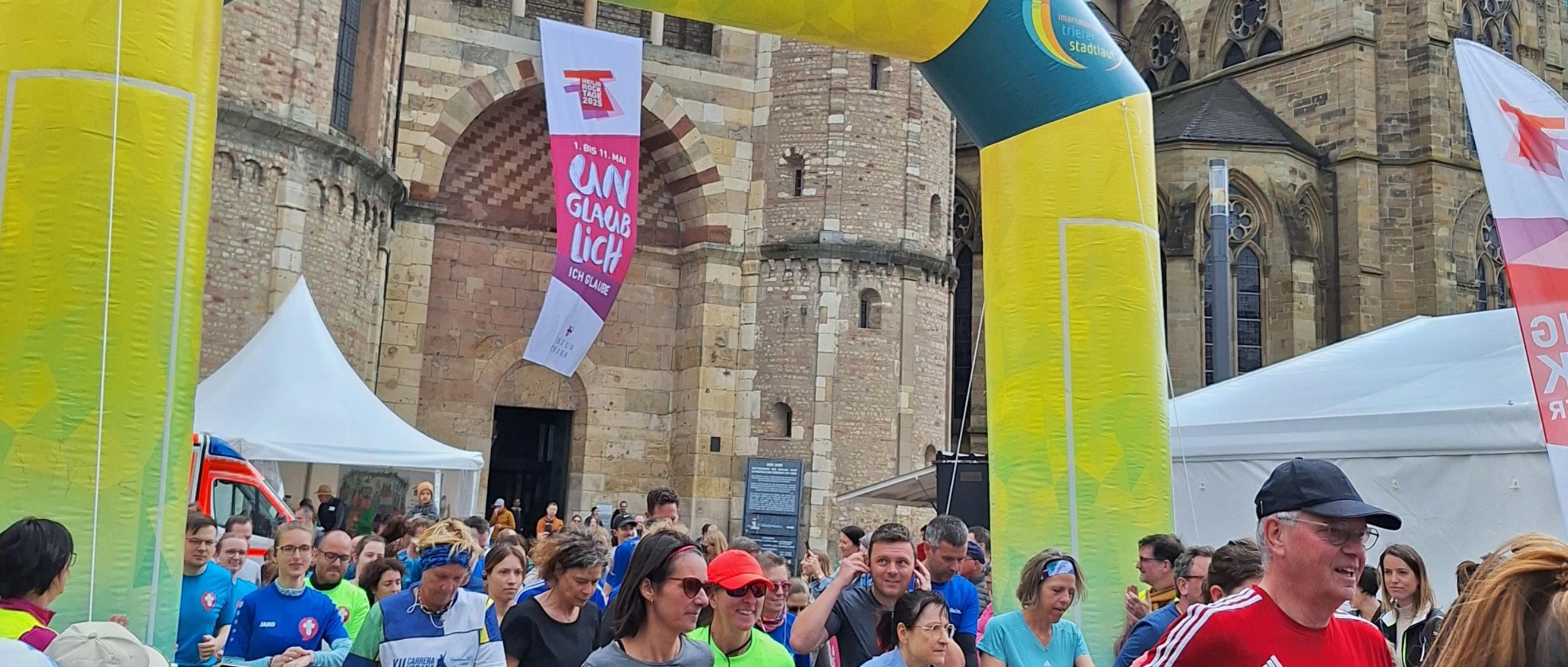 Das Bild zeigt das Ziel eines Spendenlaufes vor dem Trierer Dom. Man sieht viele Läufer.