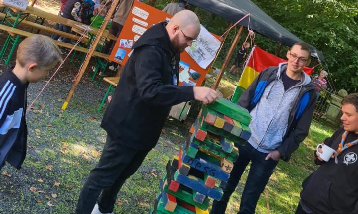 Das Bild zeigt einen Mann, dieser zieht einen Klotz bei einem Riesen-Jenga Spiel