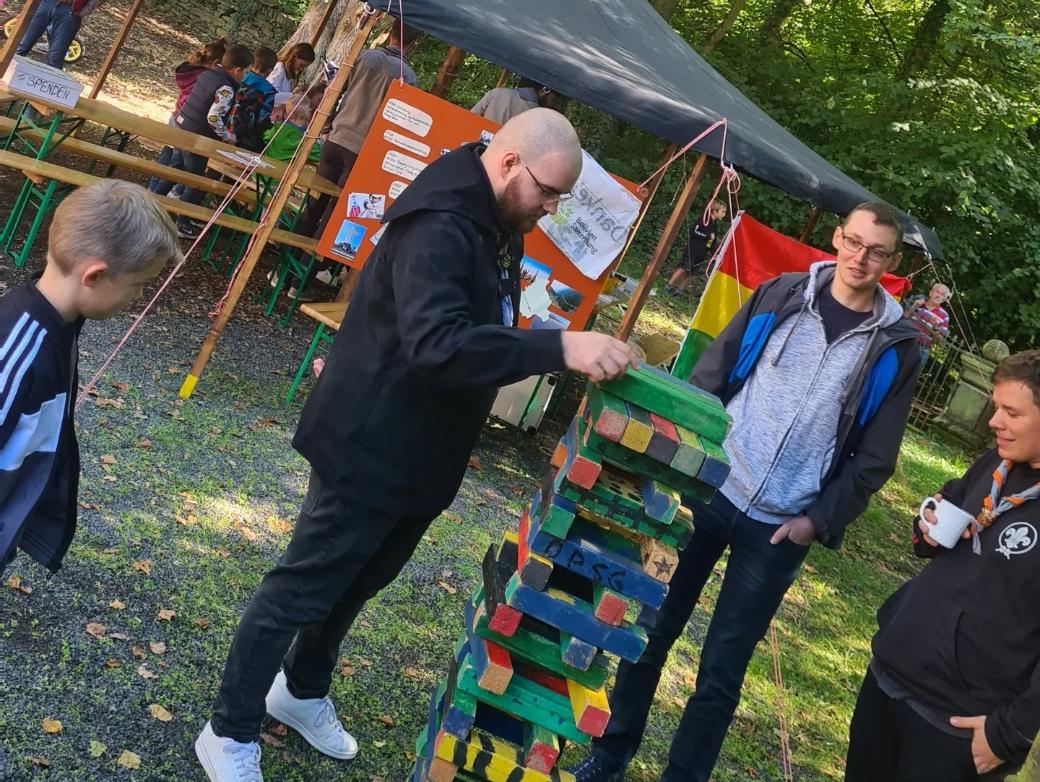 Das Bild zeigt einen Mann, dieser zieht einen Klotz bei einem Riesen-Jenga Spiel