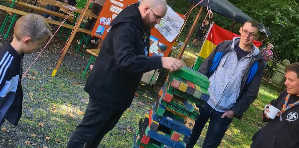 Das Bild zeigt einen Mann, dieser zieht einen Klotz bei einem Riesen-Jenga Spiel