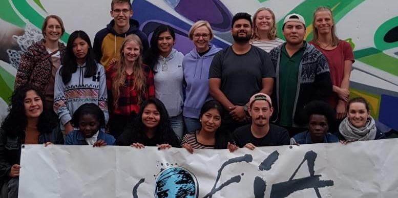 Das Bild zeigt eine Gruppe junger Menschen vor einem Banner. Es war ein Treffen von Freiwilligendienstleistenden der Soziale Friedensdienste im Ausland