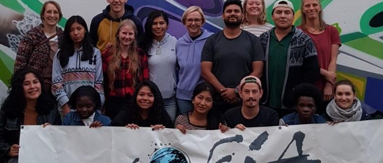 Das Bild zeigt eine Gruppe junger Menschen vor einem Banner. Es war ein Treffen von Freiwilligendienstleistenden der Soziale Friedensdienste im Ausland