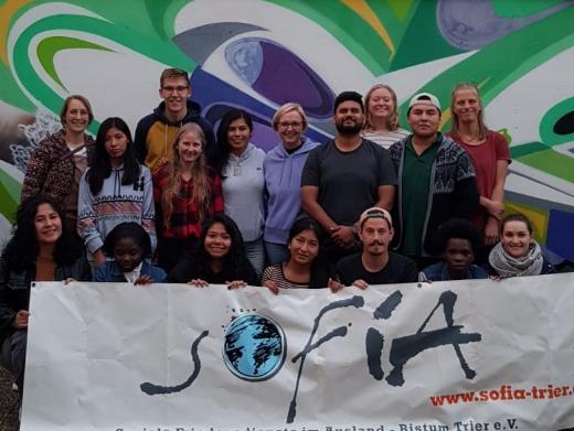 Das Bild zeigt eine Gruppe junger Menschen vor einem Banner. Es war ein Treffen von Freiwilligendienstleistenden der Soziale Friedensdienste im Ausland
