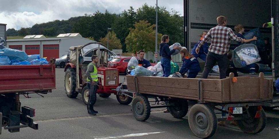 Das Bild zeigt einen Traktor mit Hänger vor einem LKW. Vom Hänger aus werden Säcke in den LKW geladen.