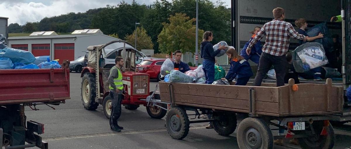 Das Bild zeigt einen Traktor mit Hänger vor einem LKW. Vom Hänger aus werden Säcke in den LKW geladen.
