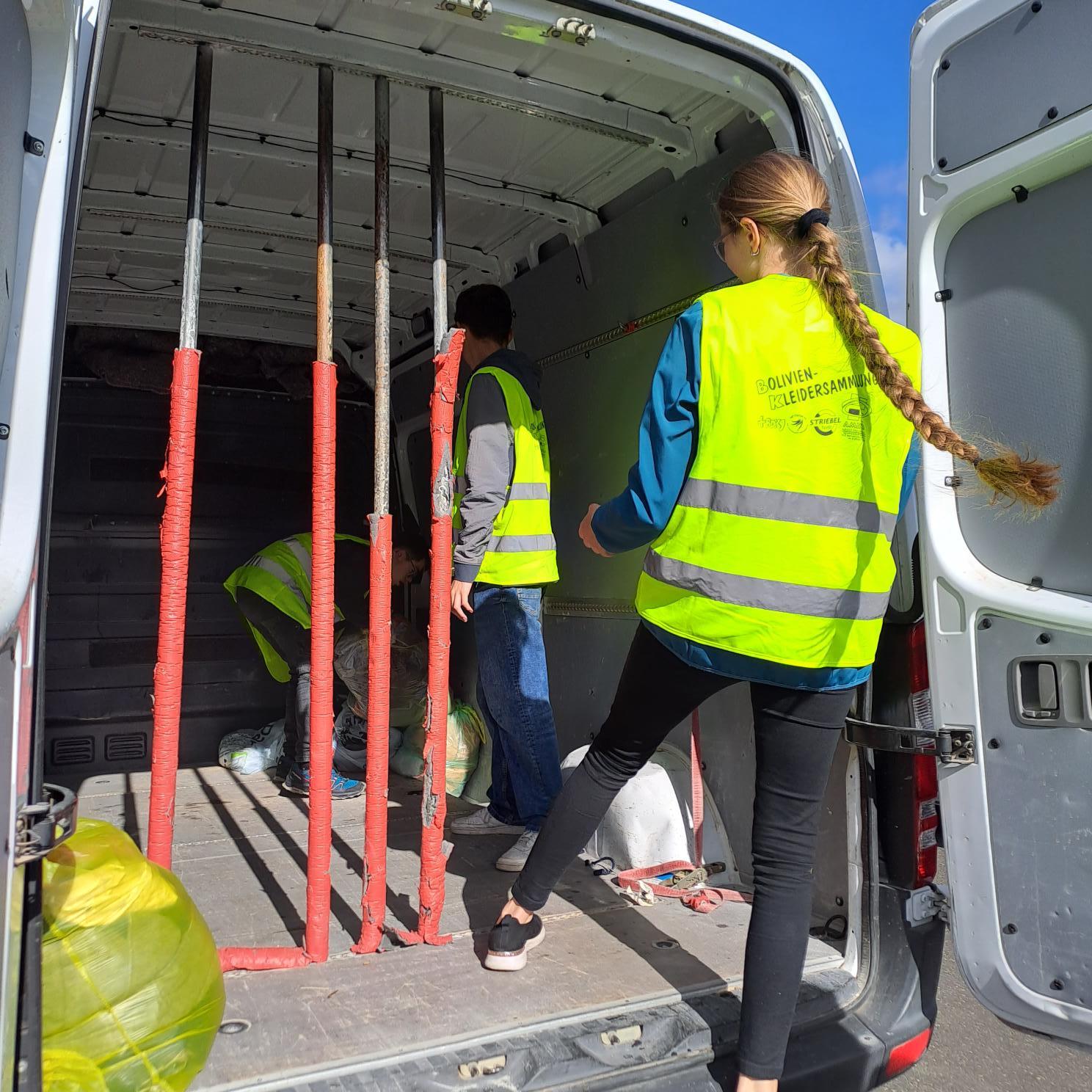 Das Bild zeigt zwei Personen die Säcke in einen Transporter laden