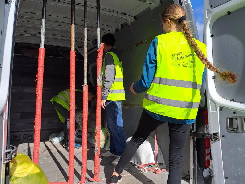 Das Bild zeigt zwei Personen die Säcke in einen Transporter laden