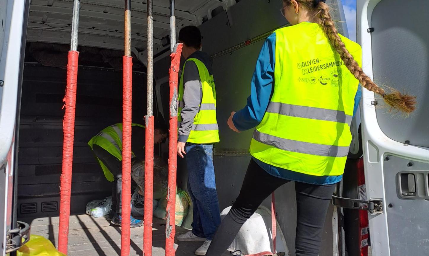 Das Bild zeigt zwei Personen die Säcke in einen Transporter laden