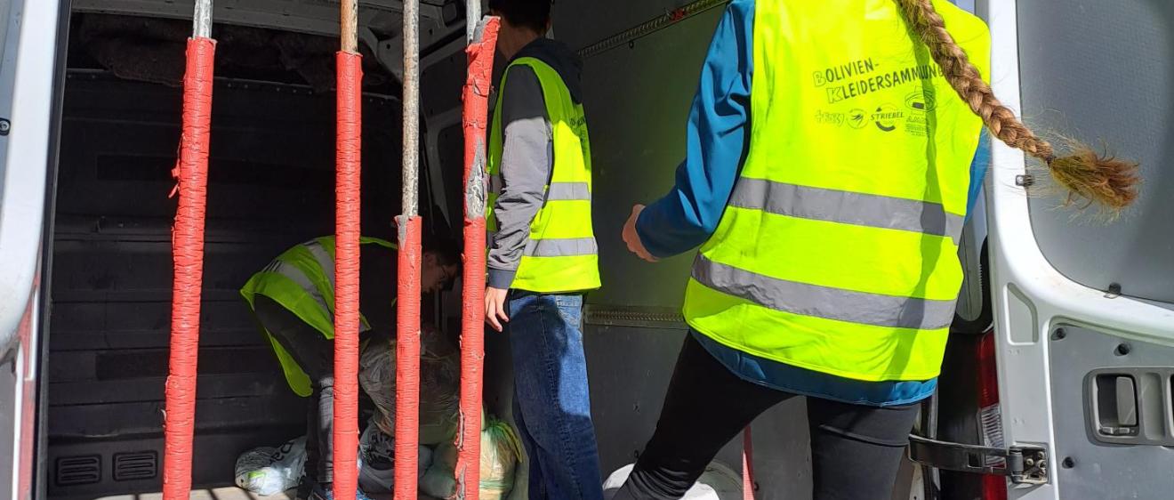 Das Bild zeigt zwei Personen die Säcke in einen Transporter laden