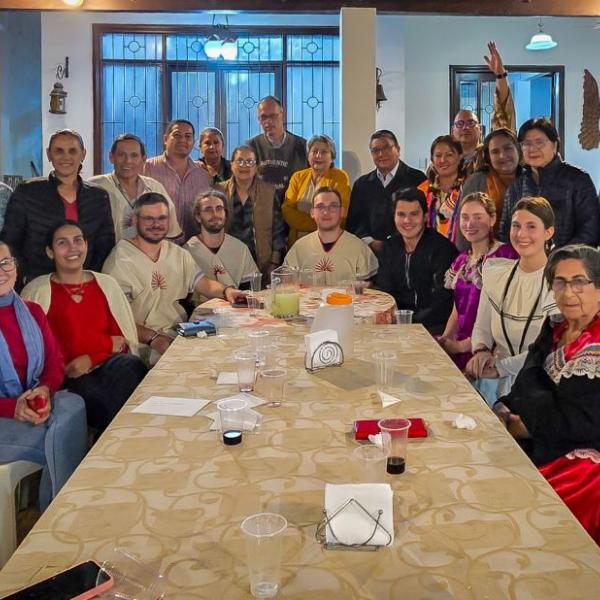 Das Bild zeigt einen langen Tisch. Am Ende versammelt sich eine Gruppe Menschen. Es ist ein Treffen der Begegnungsreise des Bistums Trier nach Bolivien.