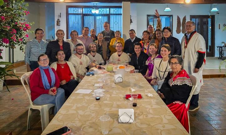 Das Bild zeigt einen langen Tisch. Am Ende versammelt sich eine Gruppe Menschen. Es ist ein Treffen der Begegnungsreise des Bistums Trier nach Bolivien.