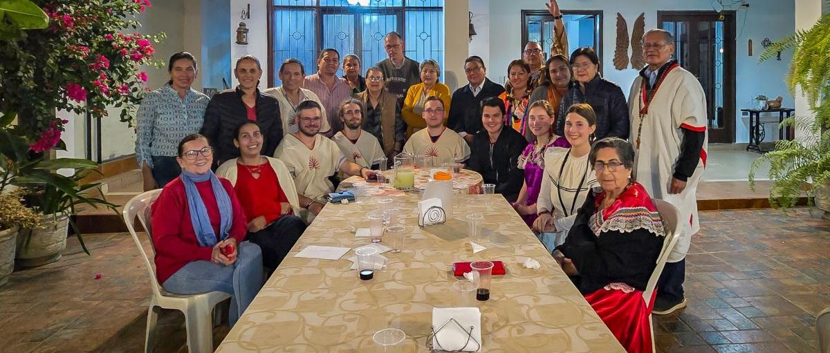 Das Bild zeigt einen langen Tisch. Am Ende versammelt sich eine Gruppe Menschen. Es ist ein Treffen der Begegnungsreise des Bistums Trier nach Bolivien.