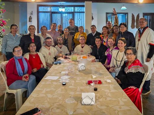 Das Bild zeigt einen langen Tisch. Am Ende versammelt sich eine Gruppe Menschen. Es ist ein Treffen der Begegnungsreise des Bistums Trier nach Bolivien.