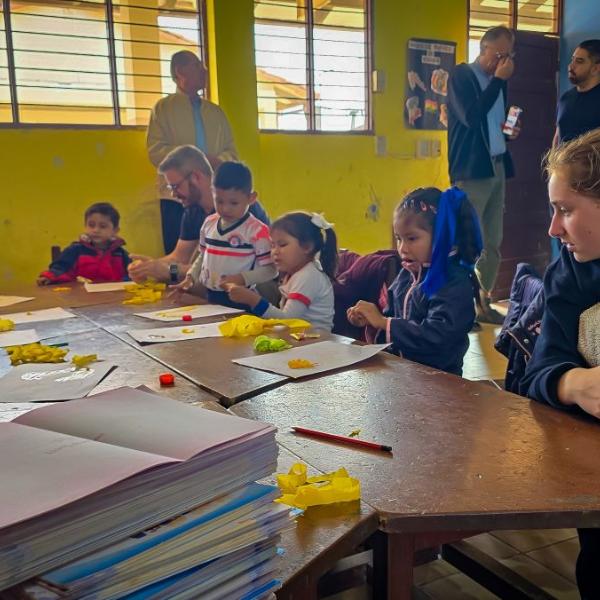 Das Bild zeigt einen Blick in eine Schulklasse in Bolivien. Eine Gruppe von Kindern lernt an Tischen.