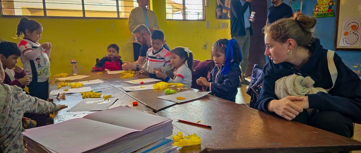 Das Bild zeigt einen Blick in eine Schulklasse in Bolivien. Eine Gruppe von Kindern lernt an Tischen.