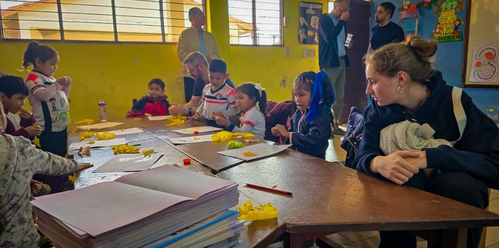 Das Bild zeigt einen Blick in eine Schulklasse in Bolivien. Eine Gruppe von Kindern lernt an Tischen.