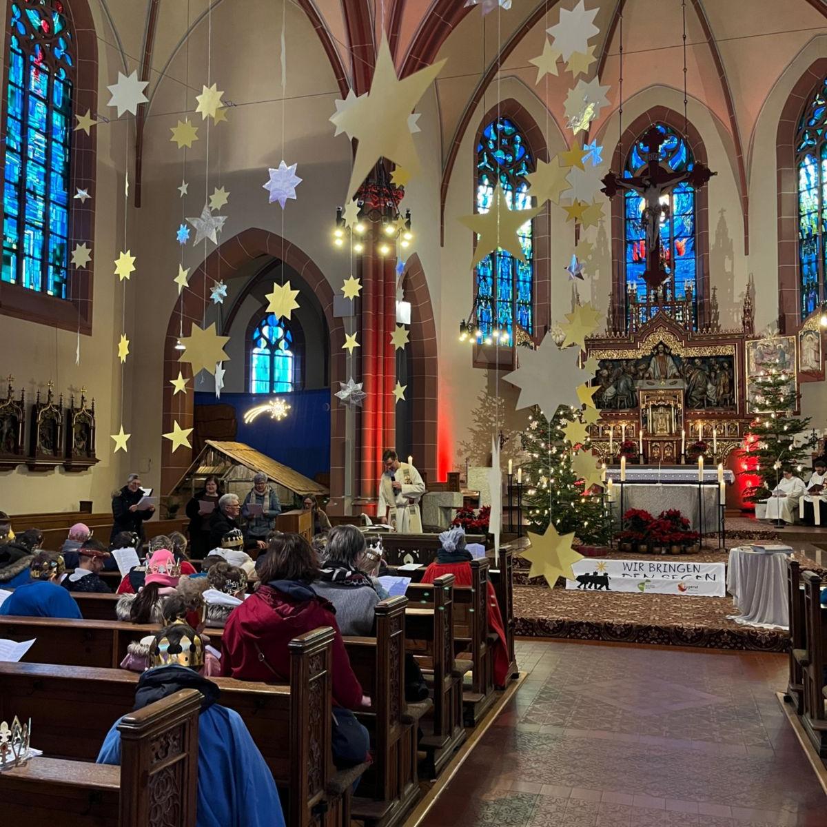Das Bild zeigt eine große Gruppe von Sternsingern im Gottesdienst von Hinten Richtung Eingang auf den Altar fotografiert.